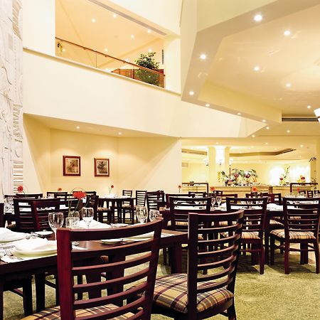 Movenpick Taba Resort & Spa Dış mekan fotoğraf The photo shows the interior of a restaurant. The space features several tables arranged with chairs, and there's a cozy ambiance created by soft lighting. The walls are designed with a decorative element, possibly a relief, and there are some framed