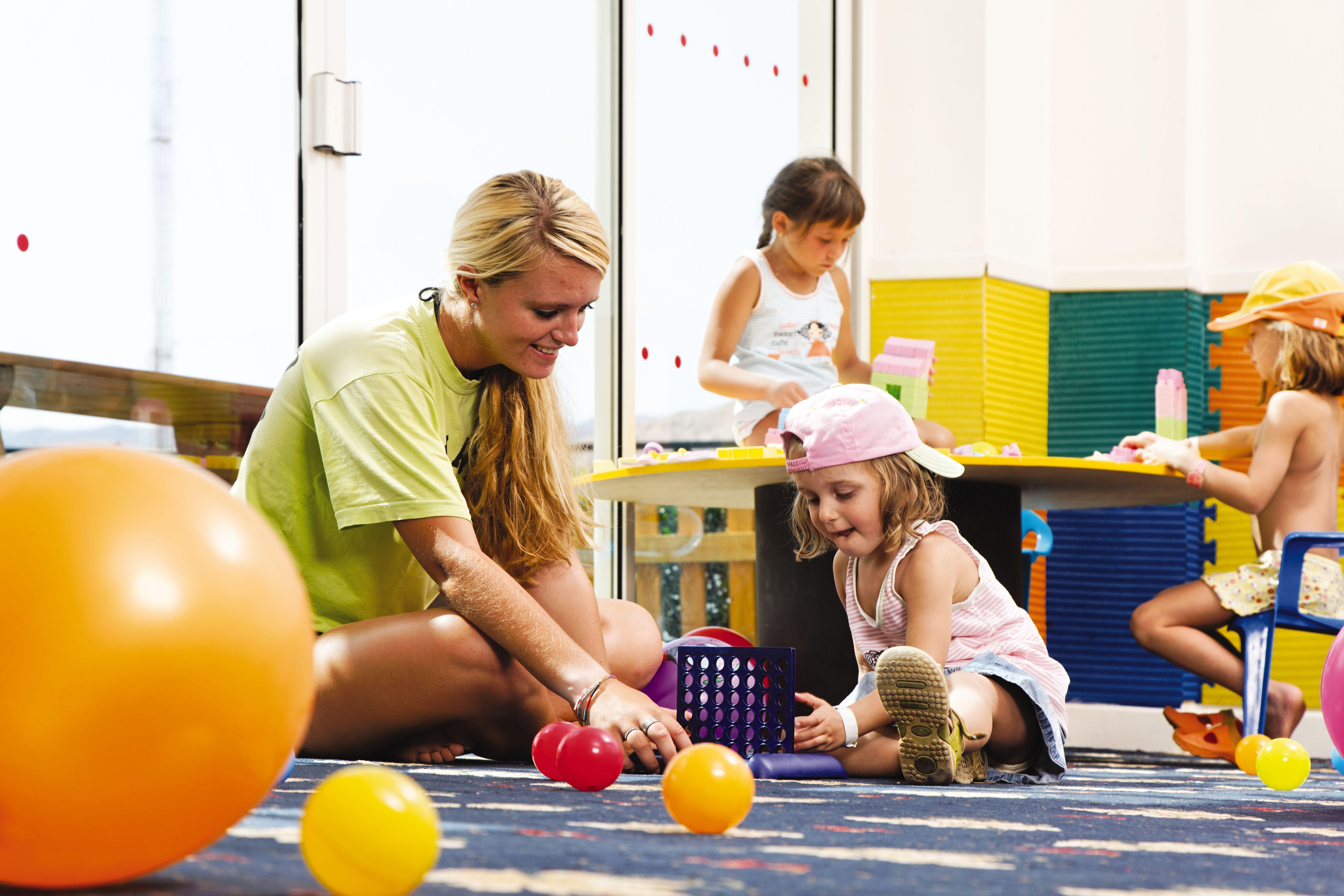 Movenpick Taba Resort & Spa Dış mekan fotoğraf The photo shows a playful and colorful indoor environment, likely a playroom or daycare. In the foreground, a young woman is sitting on the floor with a young girl, engaging in play with various colorful balls. The girl is wearing a pink cap and appe