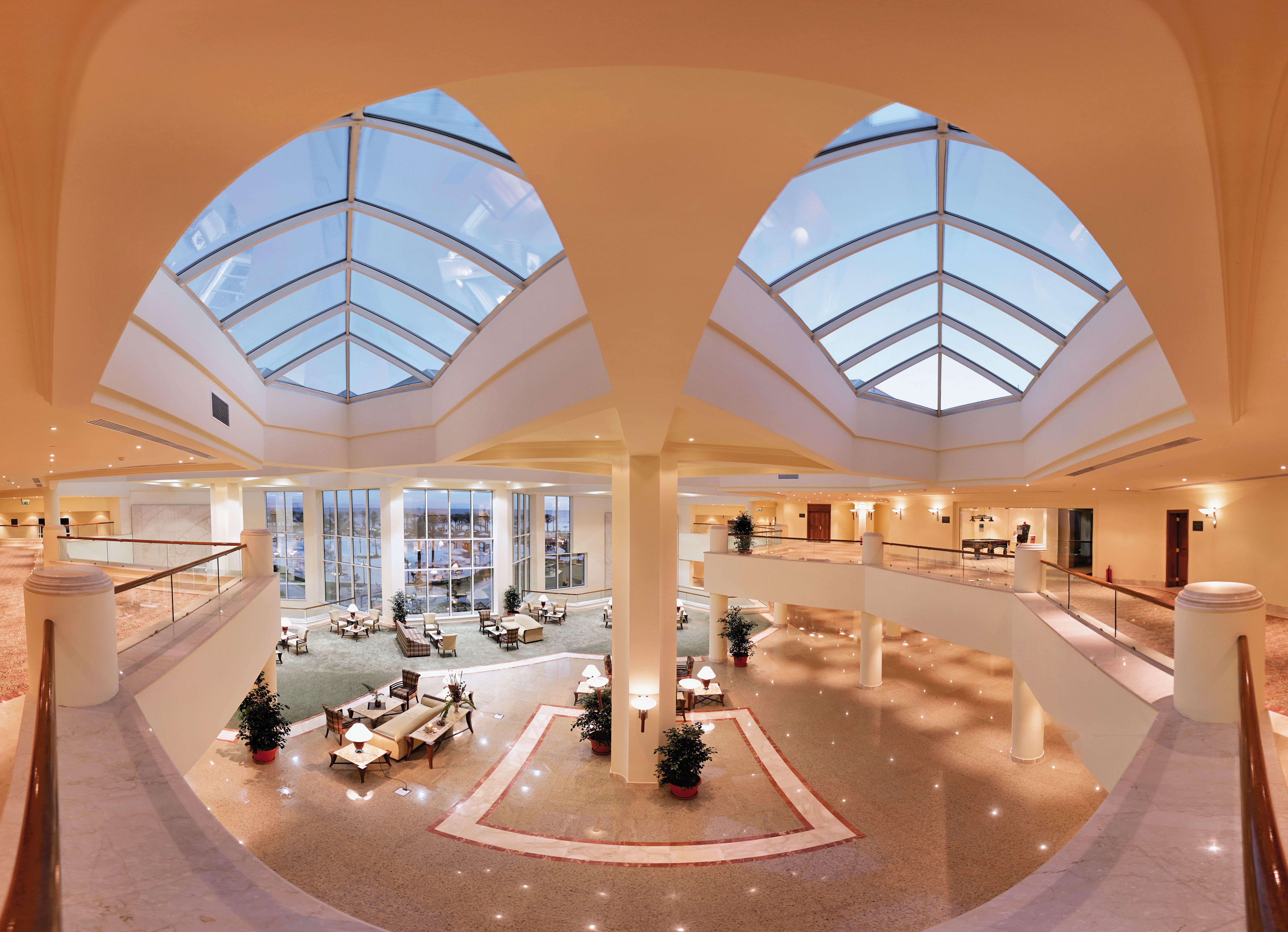 Movenpick Taba Resort & Spa Dış mekan fotoğraf The photo shows an elegant and spacious lobby area of a building, likely a hotel or a large public space. The interior features high ceilings with large skylights that allow natural light to flood the area. There are several seating arrangements, inc