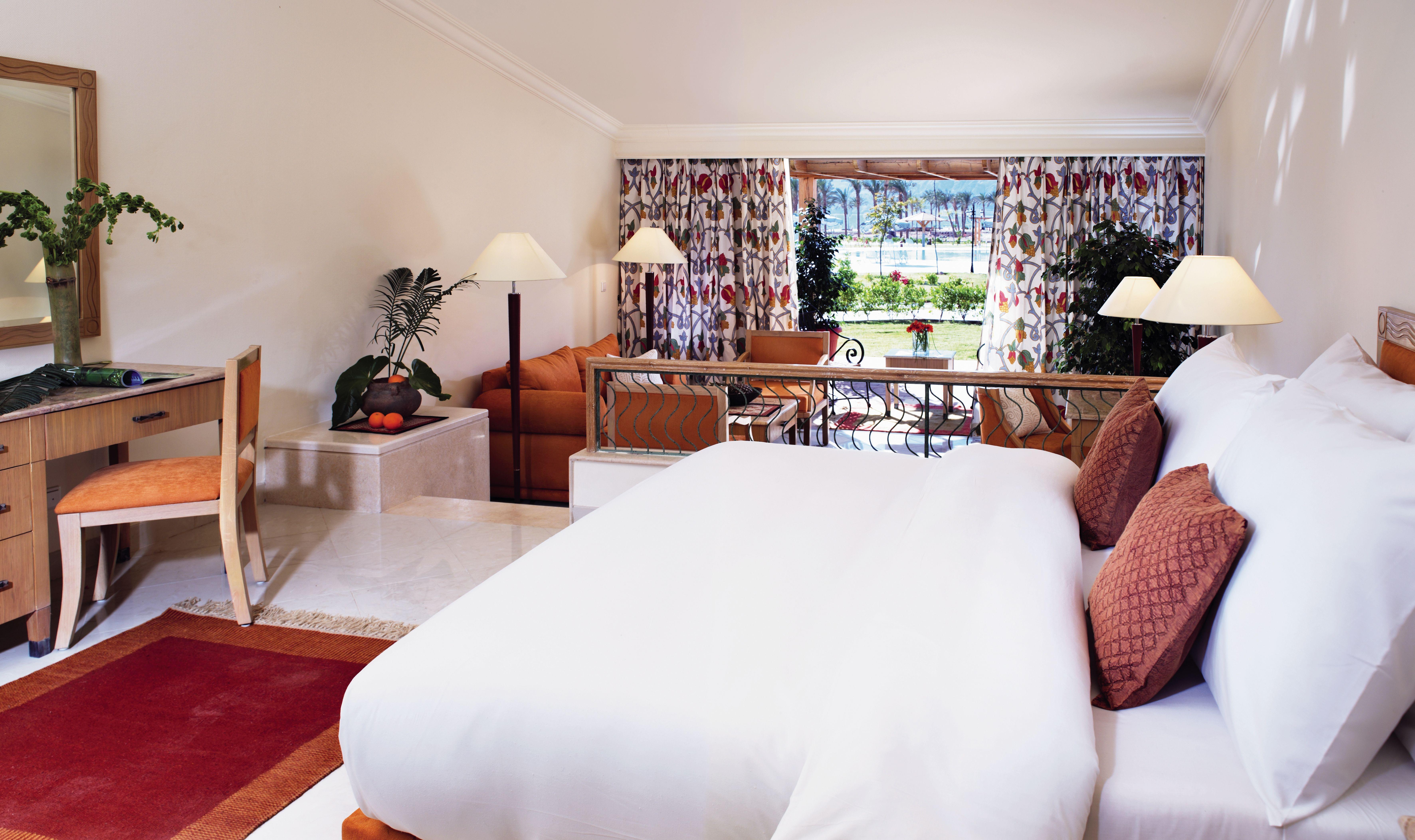 Movenpick Taba Resort & Spa Dış mekan fotoğraf The photo shows a spacious and elegantly designed hotel room or suite. In the foreground, there's a large bed with white bedding, complemented by decorative cushions. To the side, there’s a desk and chair, along with a bowl of fruit. 

In the backgro