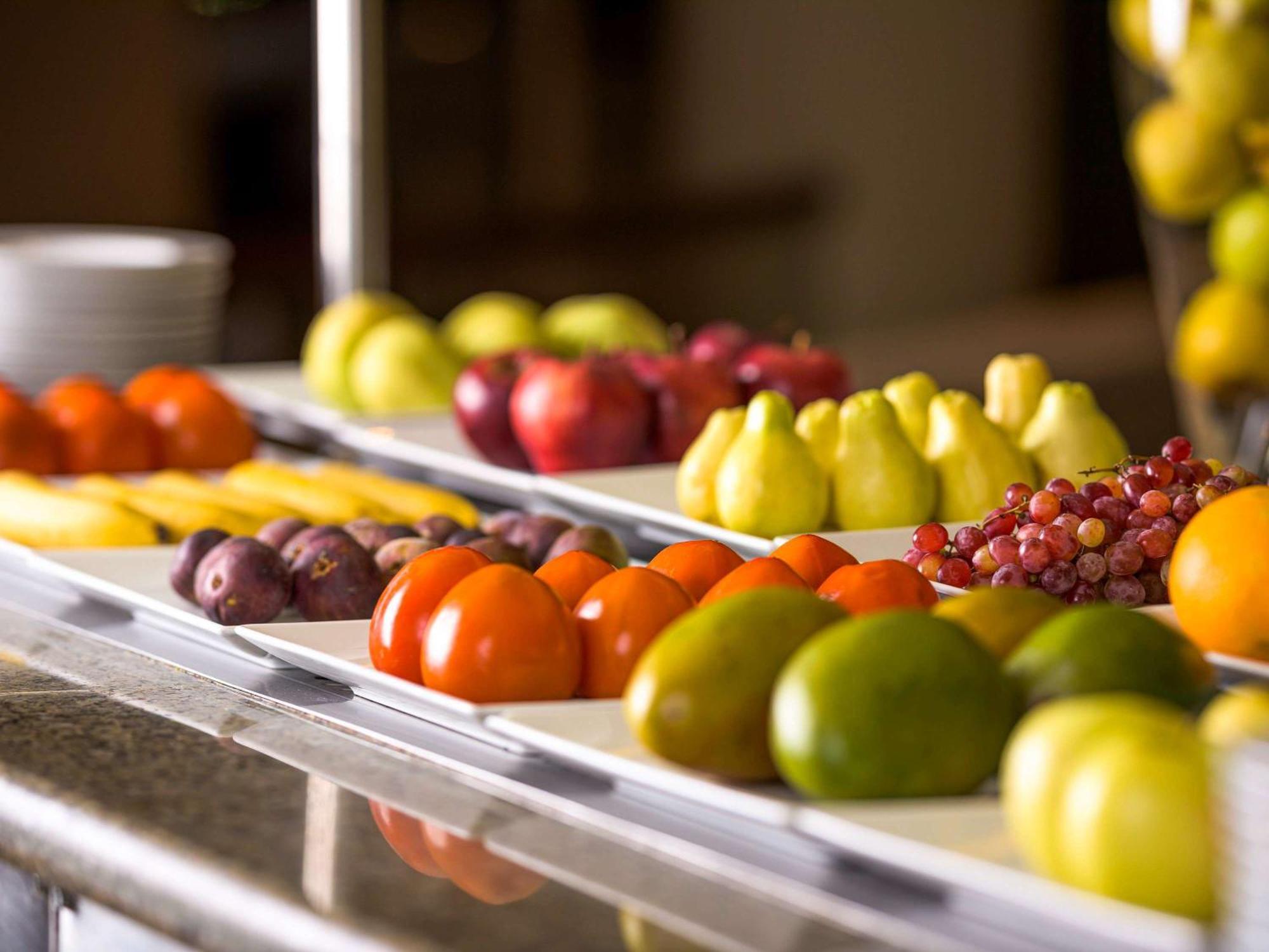 Movenpick Taba Resort & Spa Dış mekan fotoğraf The photo shows a vibrant display of assorted fruits arranged neatly on a table. There are red apples, yellow and green pears, clusters of grapes, orange-colored fruits, and small round fruits that resemble cherry tomatoes or a similar variety. The f