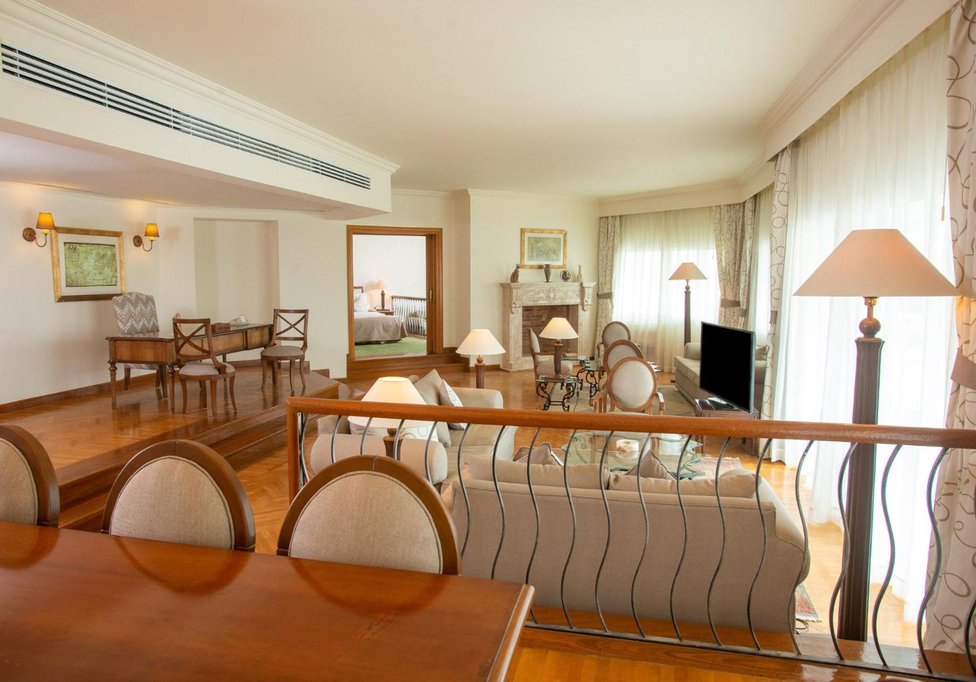 Movenpick Taba Resort & Spa Dış mekan fotoğraf The photo showcases a spacious and elegantly designed living area. In the foreground, there is a dining table with chairs, providing a formal seating arrangement. The background features a lounge area with a comfortable sofa, several side lamps, and 