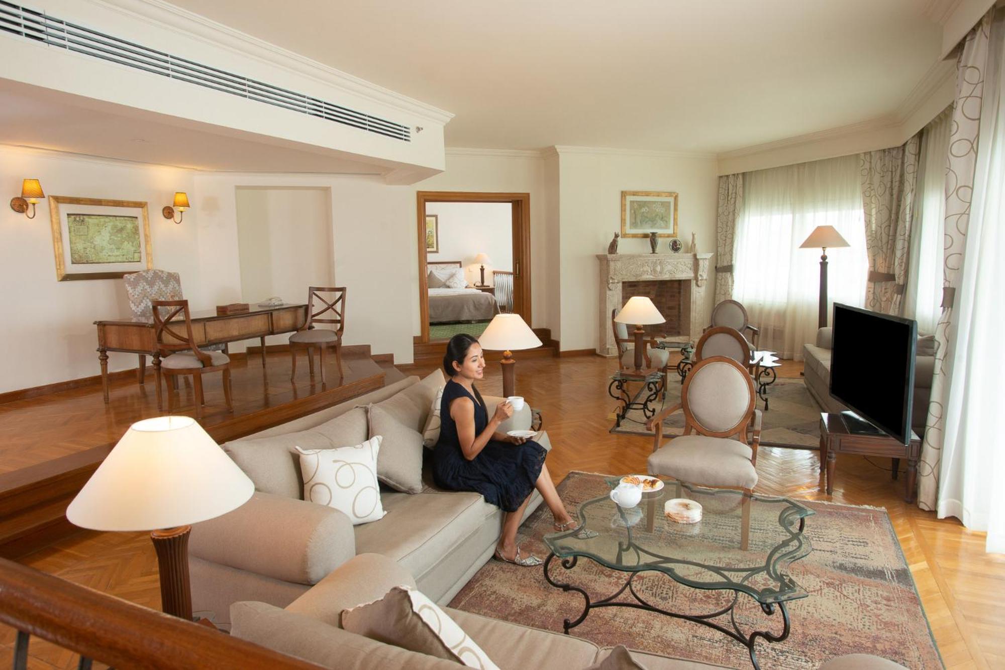 Movenpick Taba Resort & Spa Dış mekan fotoğraf The photo shows a spacious and elegantly furnished living room. There's a comfortable sofa with decorative cushions and a glass coffee table in front of it. A woman is sitting on the sofa, holding a cup, suggesting a relaxed atmosphere. To the side, 