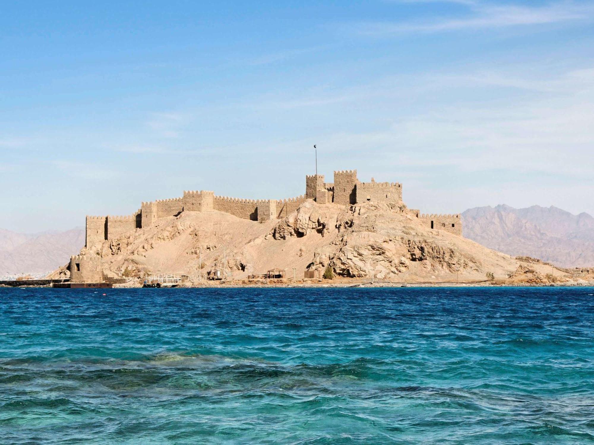 Movenpick Taba Resort & Spa Dış mekan fotoğraf The photo depicts a fortress situated on a rocky island, surrounded by clear, blue water. The fortress features high walls and seems to be atop a hill, giving it a commanding view of the surrounding area. In the background, you can see distant mounta