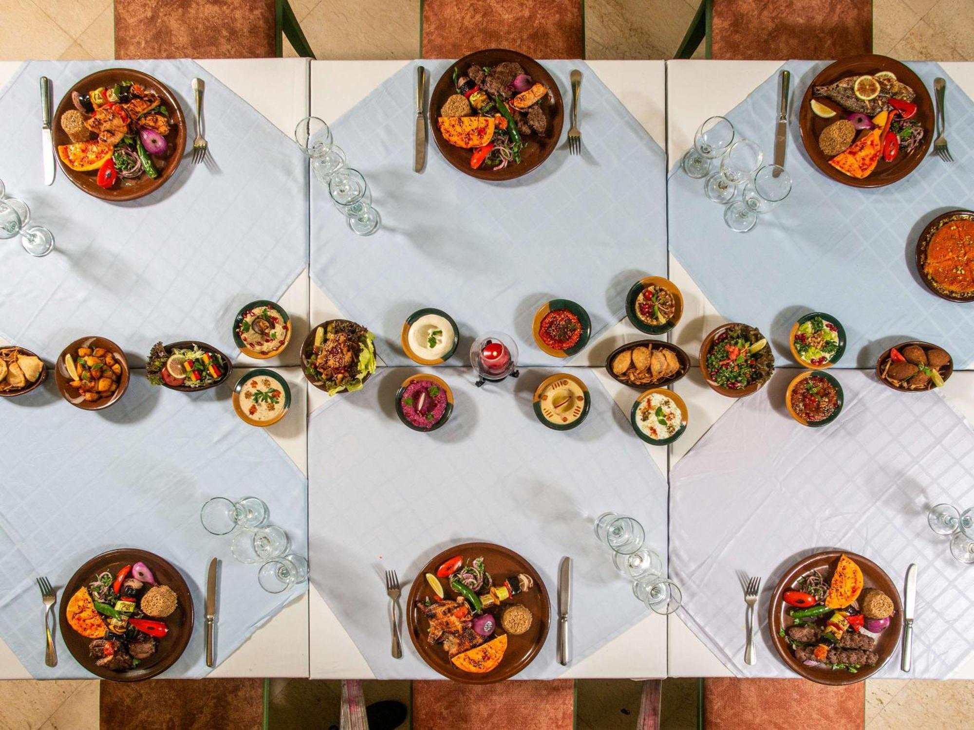 Movenpick Taba Resort & Spa Dış mekan fotoğraf The photo shows a beautifully arranged dining table set for a feast. There are multiple dishes displayed on the table, each in circular bowls. The table is adorned with a light blue tablecloth, creating a serene atmosphere. Various colorful dishes fe