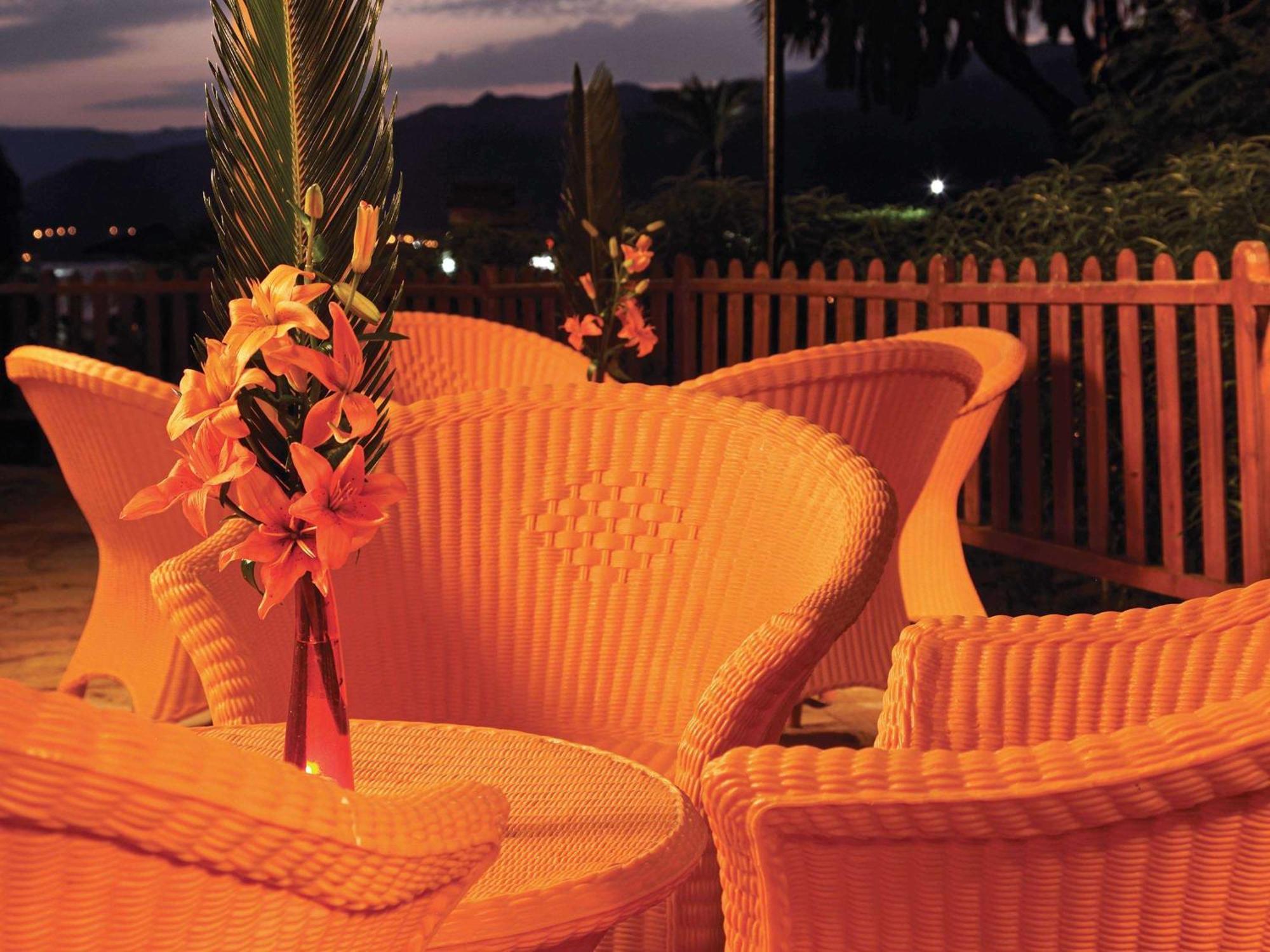 Movenpick Taba Resort & Spa Dış mekan fotoğraf The photo shows a cozy outdoor setting with a round table surrounded by several wicker chairs. Each chair has a unique, curvy design and is bathed in warm, soft lighting, creating an inviting atmosphere. In the center of the table, there is a decorat