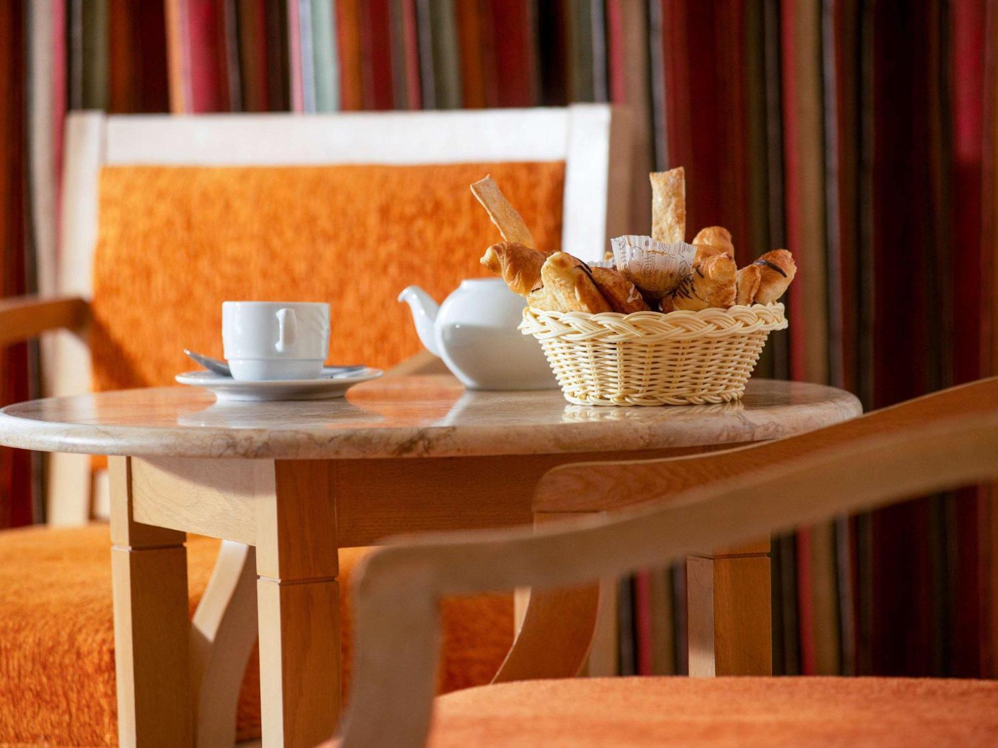 Movenpick Taba Resort & Spa Dış mekan fotoğraf The photo features a small table with a light-colored marble top. On the table, there's a white cup and saucer, along with a teapot. In the center, there’s a woven basket filled with various types of breadsticks or snacks. The background includes cha