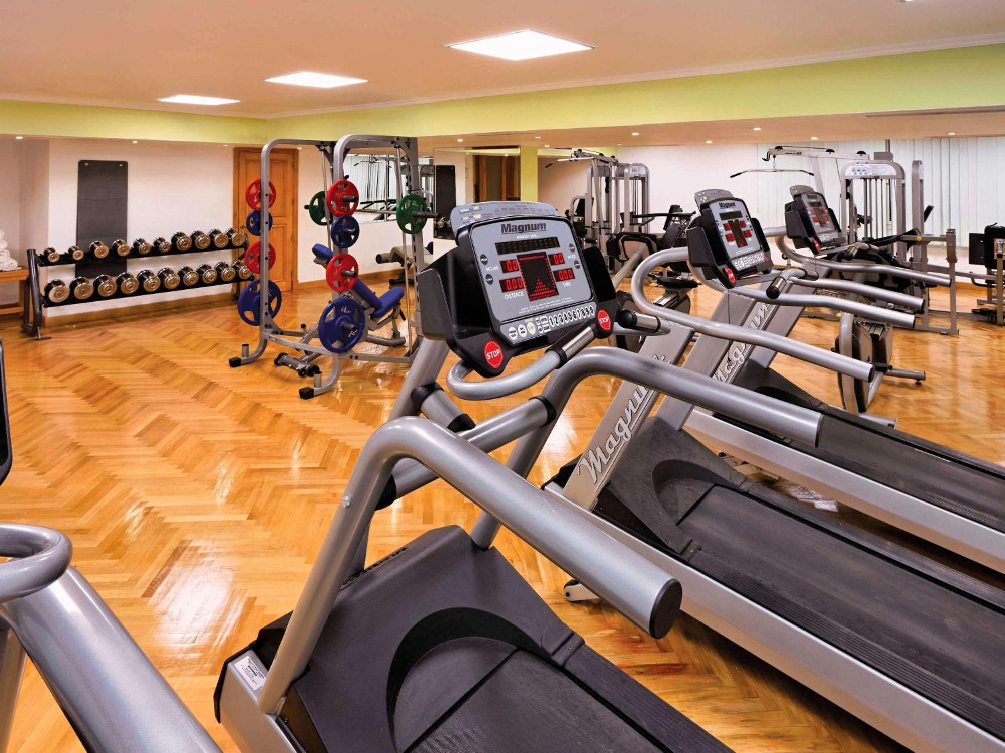 Movenpick Taba Resort & Spa Dış mekan fotoğraf The photo shows a modern gym interior featuring several exercise machines and equipment. In the foreground, there are multiple treadmills lined up, each equipped with electronic displays. In the background, there are various weightlifting equipment a