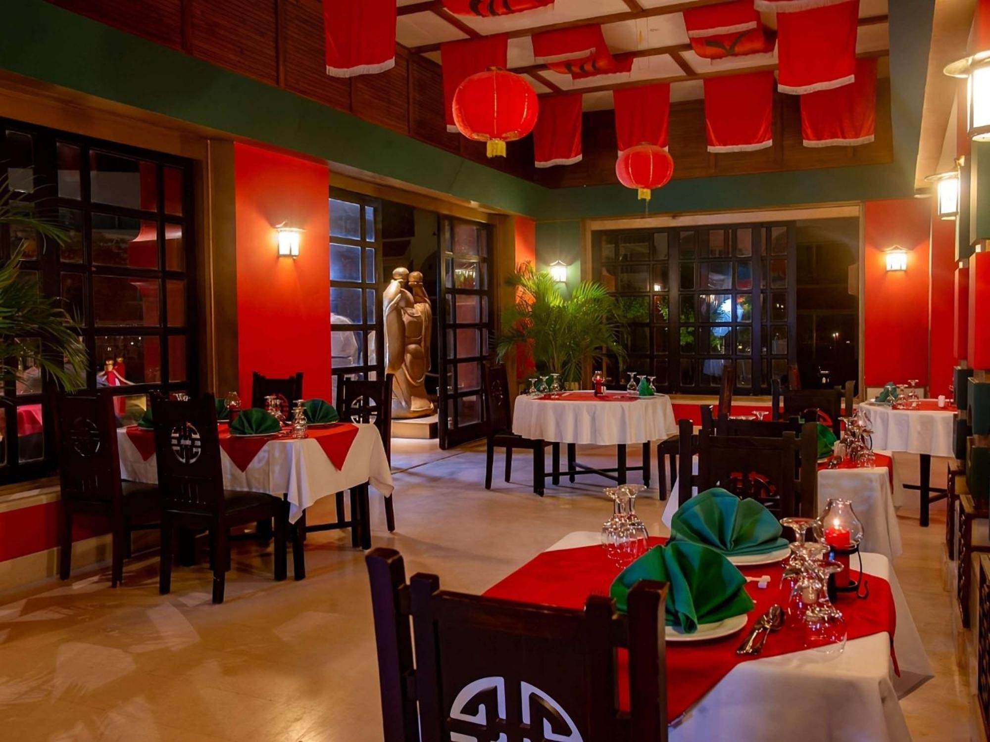 Movenpick Taba Resort & Spa Dış mekan fotoğraf The photo shows a stylish dining area with a distinctive Asian-inspired decor. The space features tables set with white and red tablecloths, and elegant tableware, including glasses and napkins. The walls are painted in rich, vibrant colors, primaril