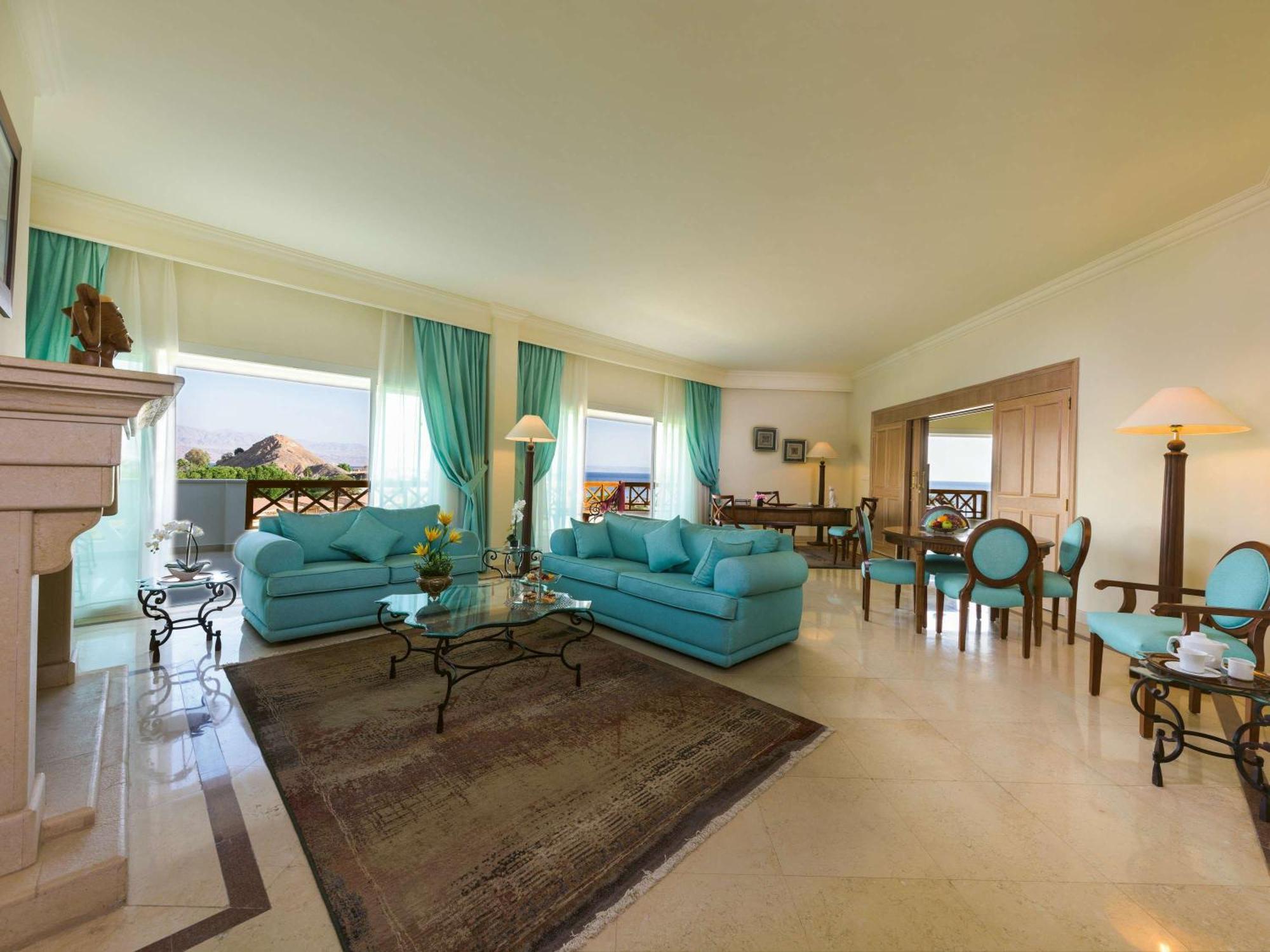 Movenpick Taba Resort & Spa Dış mekan fotoğraf The photo shows a spacious and elegantly designed living area. It features two light blue sofas arranged around a glass coffee table, creating a cozy seating area. There are large windows dressed with sheer curtains, allowing natural light to fill th