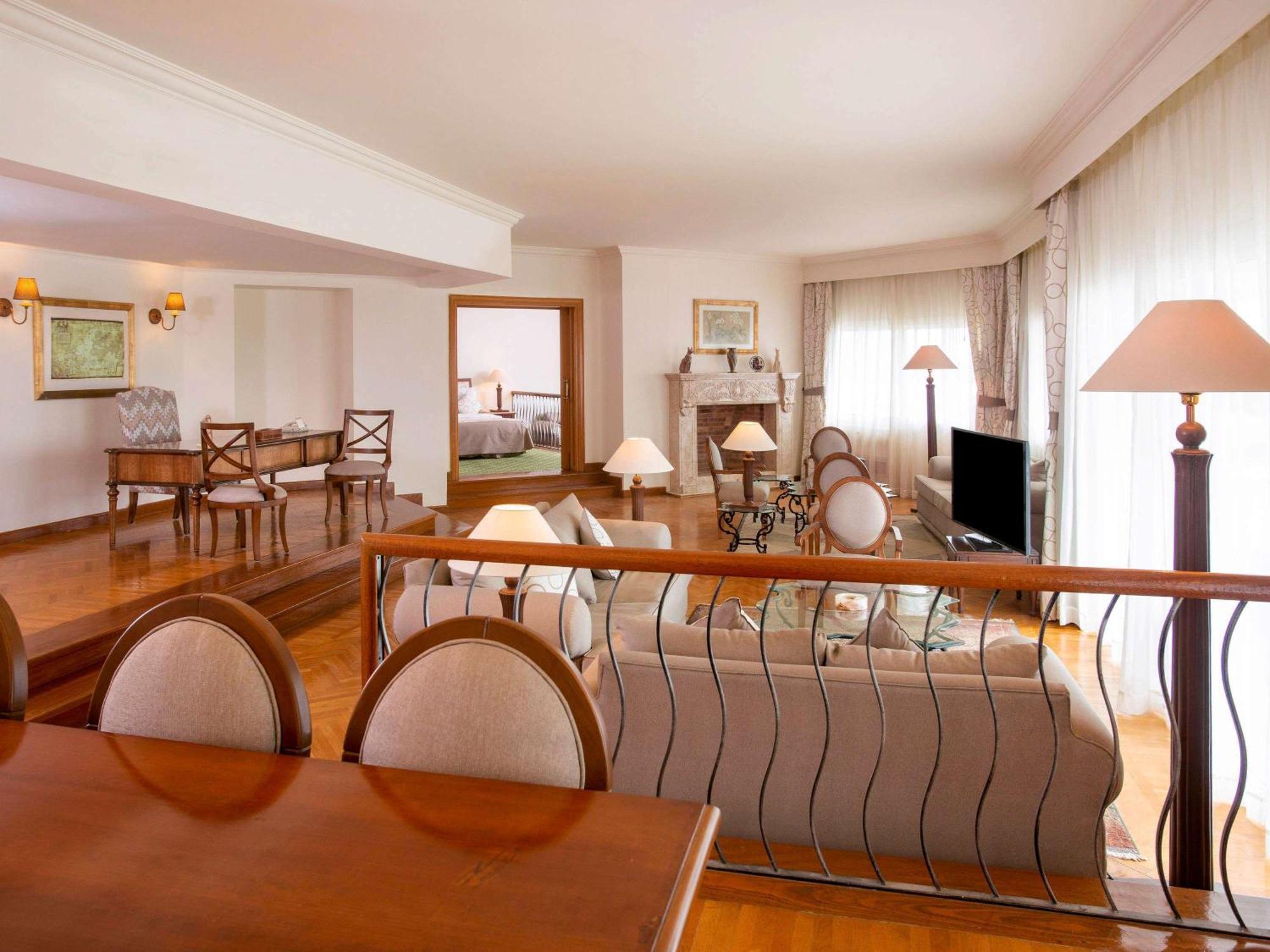 Movenpick Taba Resort & Spa Dış mekan fotoğraf The photo shows a spacious and elegantly designed living area. It features a comfortable seating arrangement with sofas and chairs, along with a dining table that has circular chairs. The room is well-lit, with large windows covered by sheer curtains