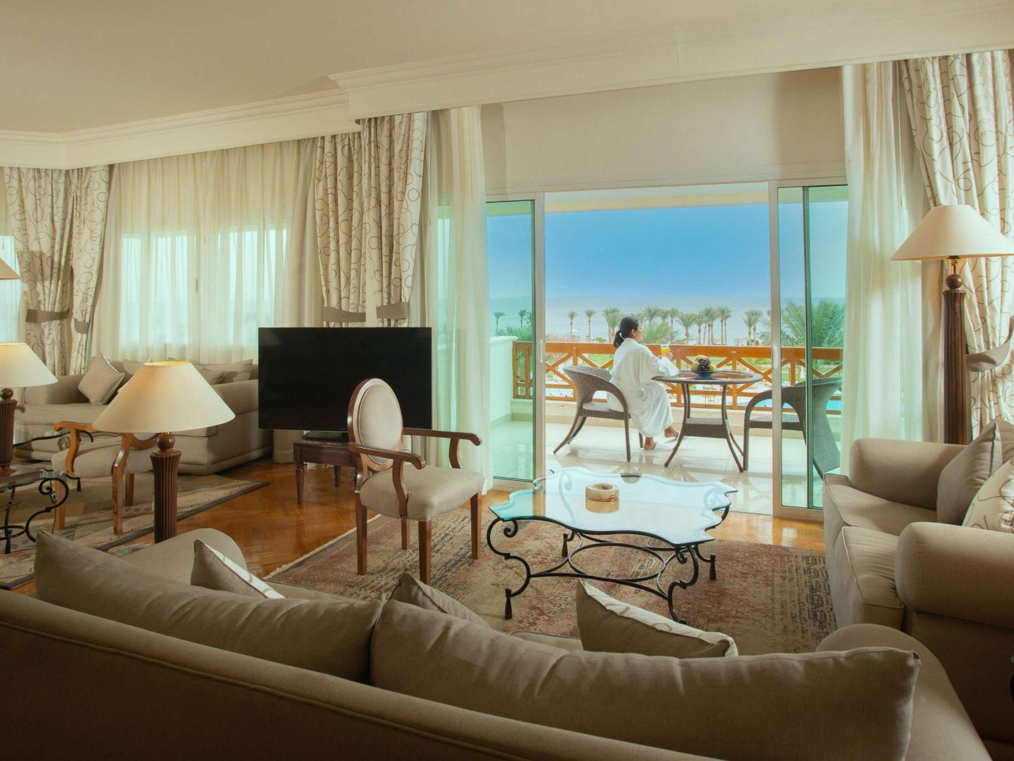 Movenpick Taba Resort & Spa Dış mekan fotoğraf The photo depicts a luxurious hotel suite. Inside, there is a spacious living area with elegant furnishings, including a large sofa, stylish armchairs, and a glass coffee table. A flat-screen TV is positioned in one corner. The large windows allow na